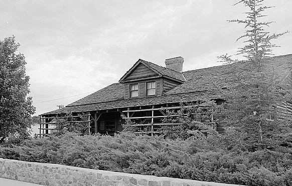 The log Governor’s Mansion in Prescott with a porch, dormer, shrubs and stone wall